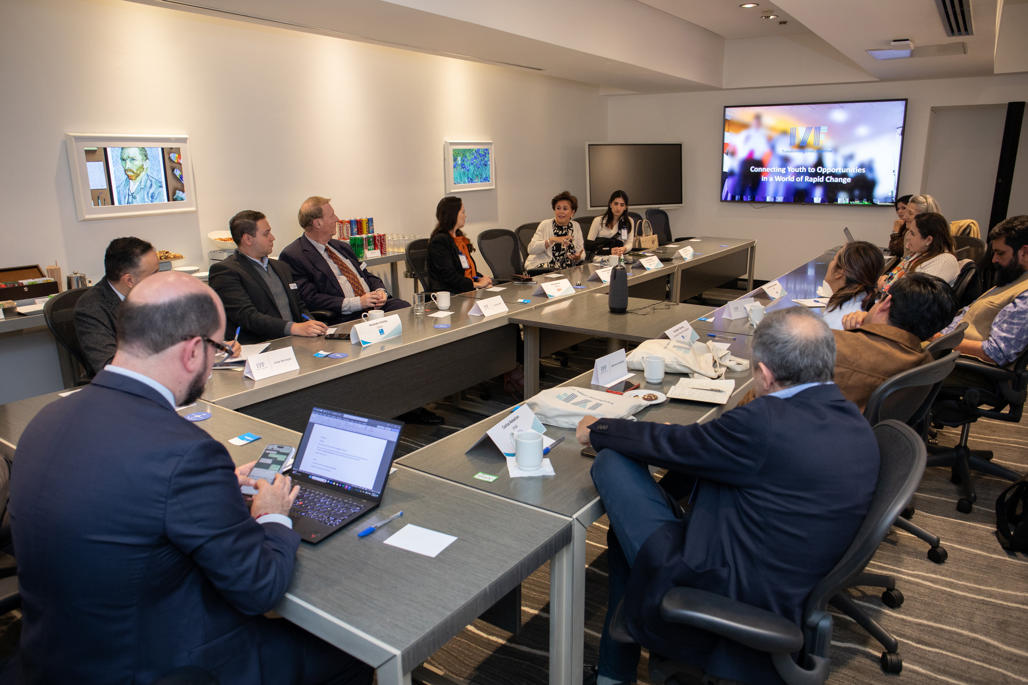 People engaged around a conference room table while large screen TV displays a slide cover image